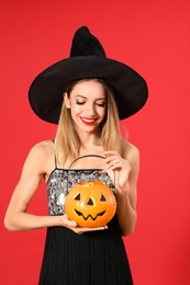 Beautiful woman wearing witch costume with Jack O'Lantern candy container on red background. Halloween party