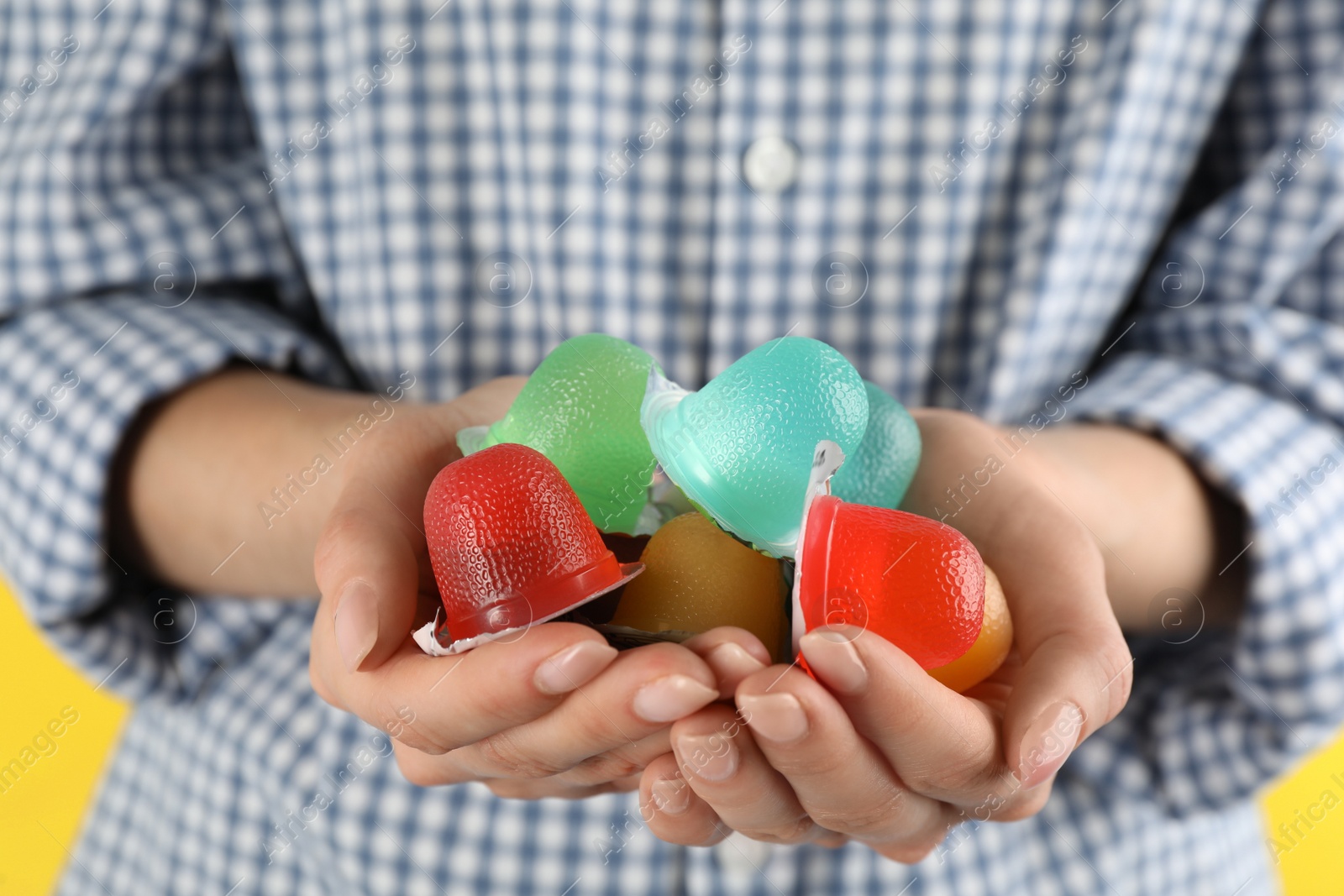 Photo of Woman holding many tasty bright jelly cups on yellow background, closeup