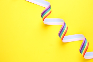 Photo of Top view of rainbow ribbon on yellow background, space for text. Gay symbol