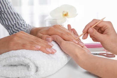 Photo of Manicurist preparing client's fingernail cuticles in salon, closeup