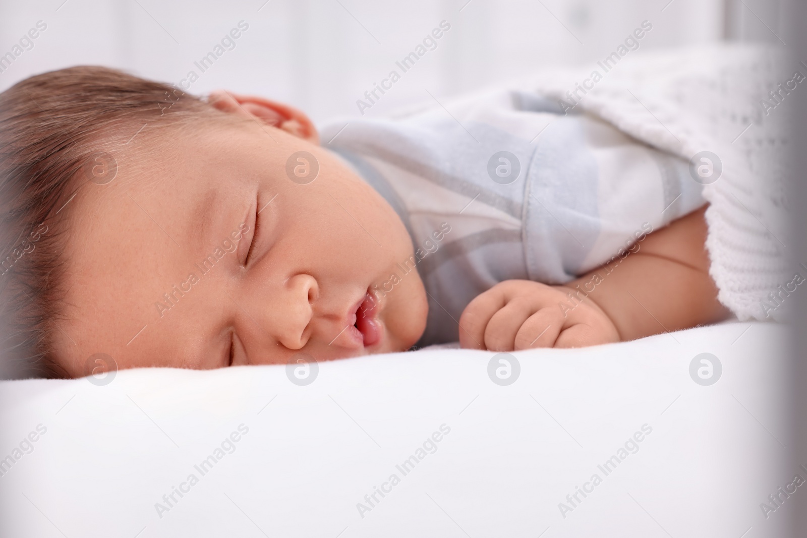 Photo of Cute newborn baby sleeping under white plaid on bed, closeup