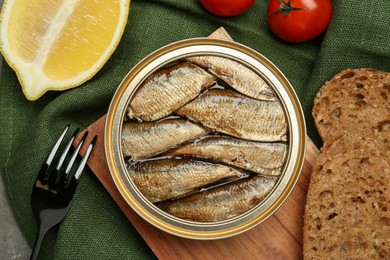 Photo of Canned sprats, lemon, tomatoes, bread and fork on table, flat lay