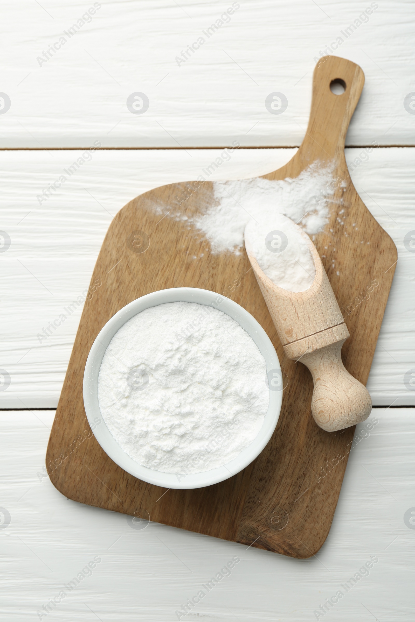 Photo of Baking powder in bowl and scoop on white wooden table, top view