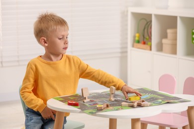Cute little boy playing with set of wooden road signs and cars at table indoors, space for text. Child's toy