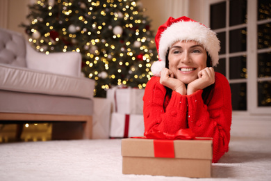 Photo of Beautiful woman with gift box in living room, space for text. Christmas celebration