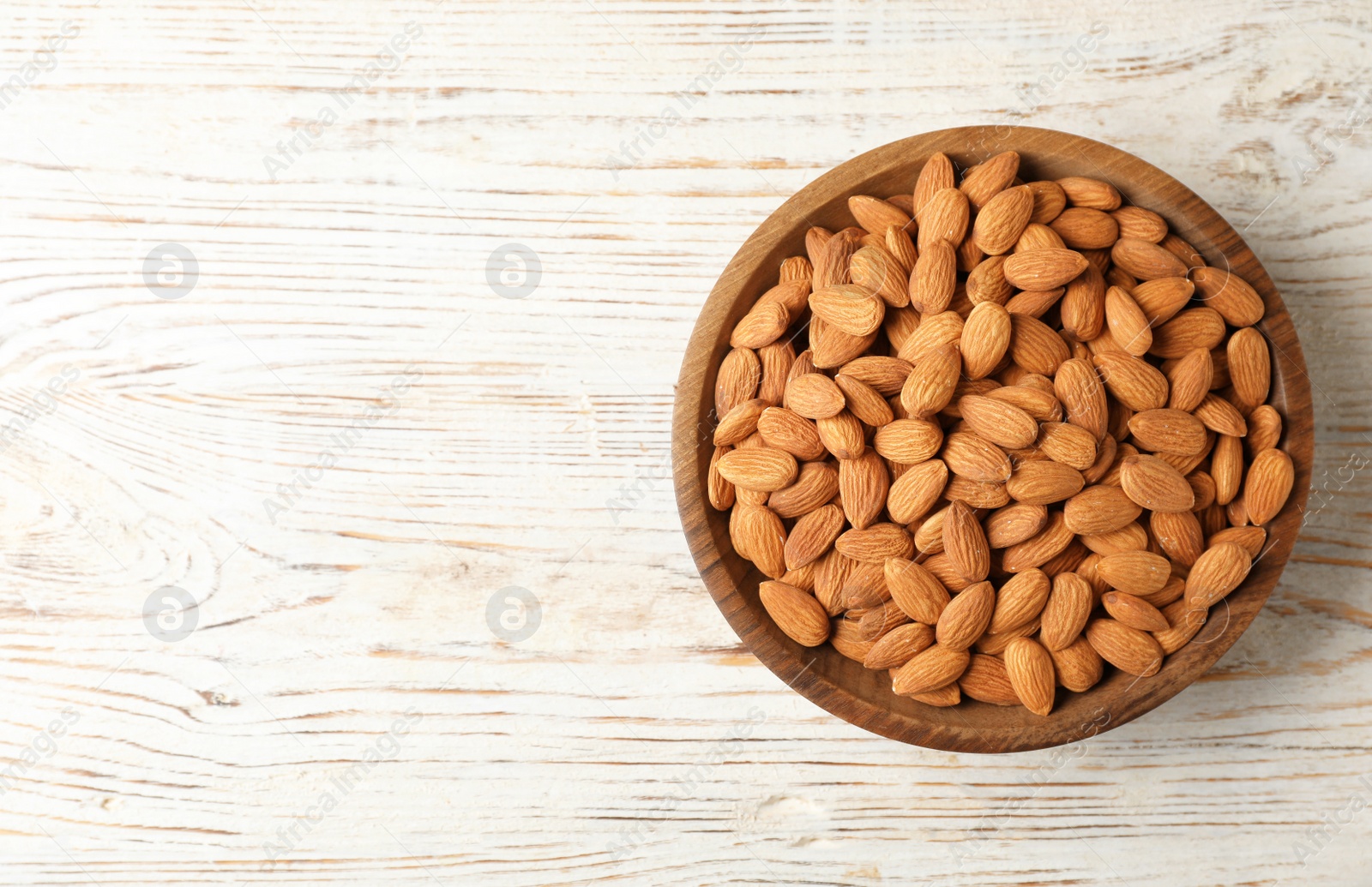 Photo of Tasty organic almond nuts in bowl and space for text on table, top view