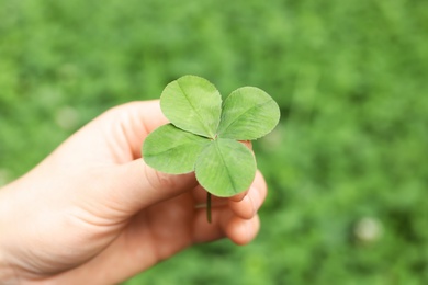 Woman holding four-leaf clover outdoors, closeup