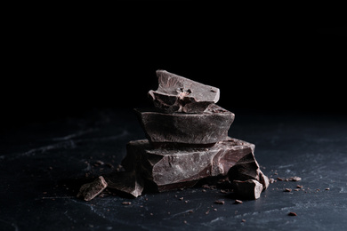 Photo of Pieces of tasty dark chocolate on black table, closeup