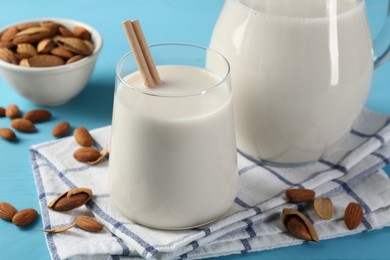 Glass of almond milk, jug and almonds on light blue wooden table, closeup
