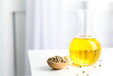 Bottle with hemp oil and seeds on white table indoors. Space for text