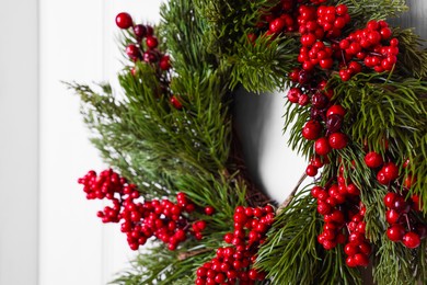 Beautiful Christmas wreath with red berries hanging on white door, closeup