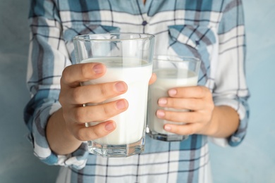 Woman holding glasses of hemp milk on light blue background, closeup