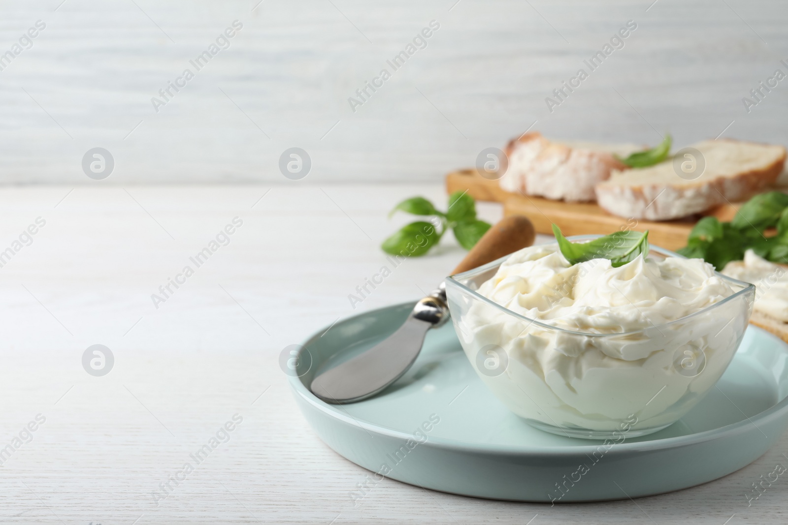 Photo of Tasty cream cheese with basil on white wooden table. Space for text
