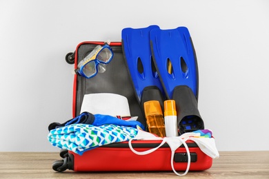 Open suitcase with clothing and swimming accessories on table