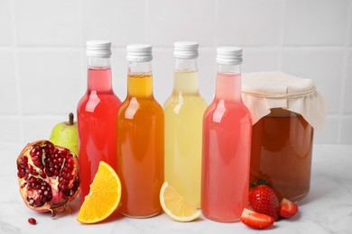 Photo of Delicious kombucha in glass bottles, jar and fresh fruits on white marble table