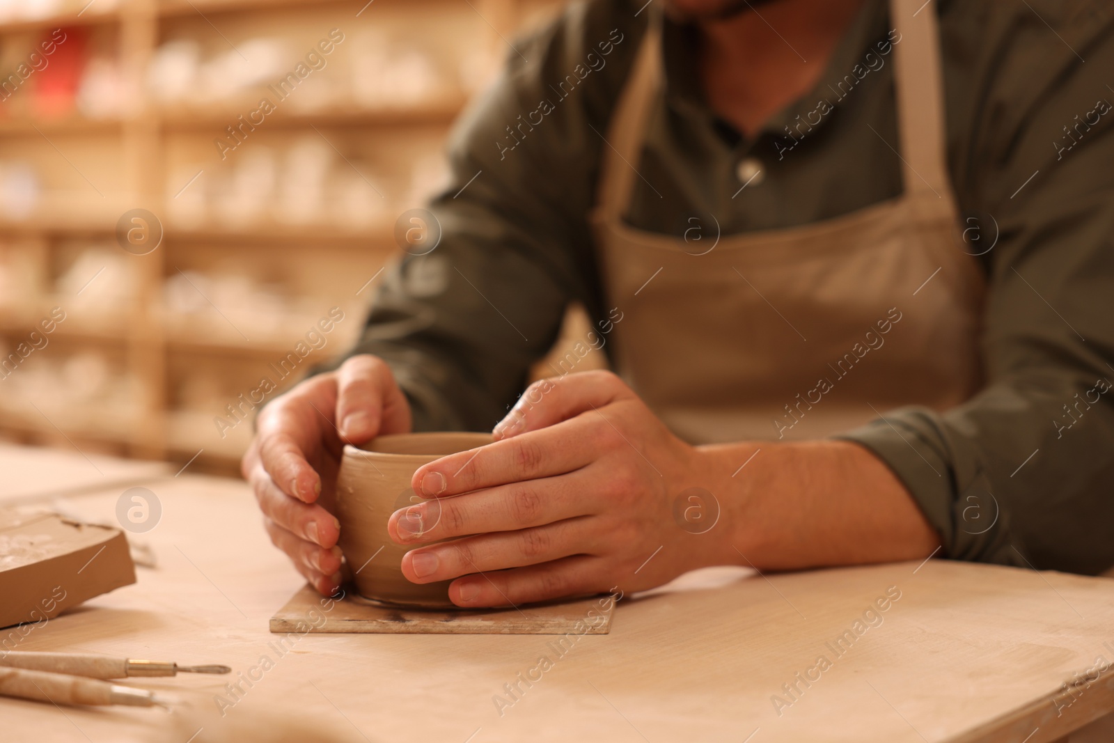 Photo of Clay crafting. Man making bowl at table indoors, closeup