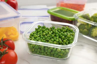 Containers with green peas and fresh products on white marble table, closeup. Food storage