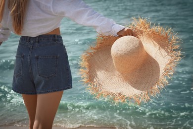 Photo of Young woman with straw hat near sea on sunny day in summer, closeup back view
