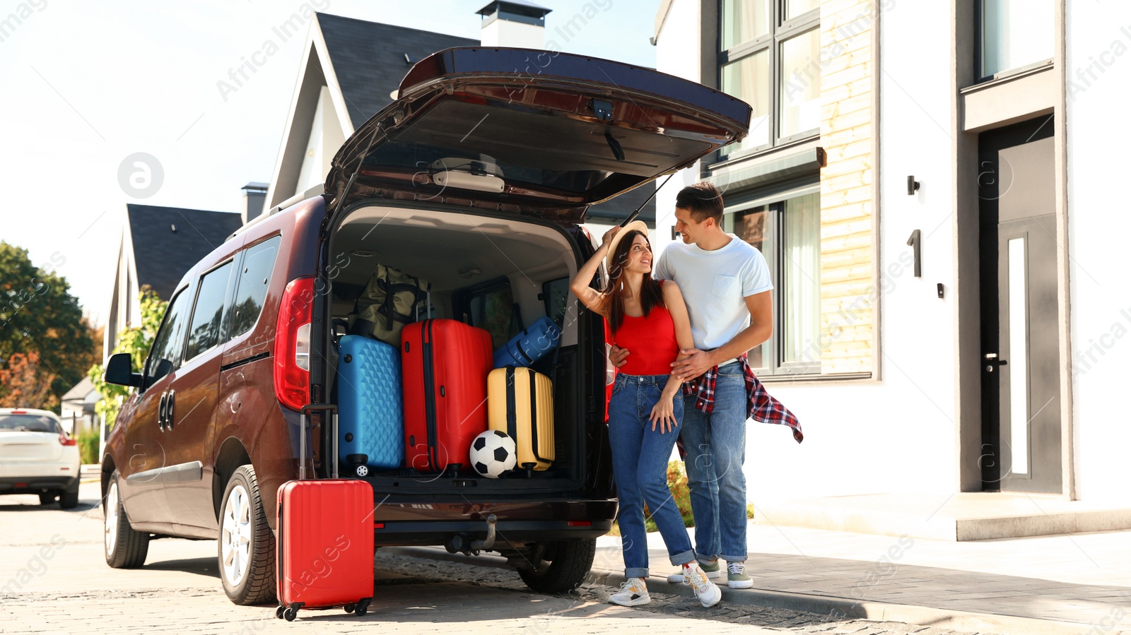 Photo of Young couple near car with suitcases in trunk outdoors. Moving day