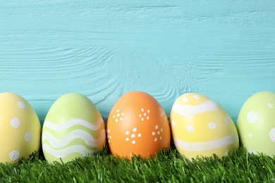 Photo of Colorful painted Easter eggs on green grass against wooden background, space for text