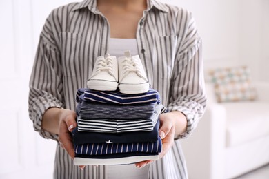 Woman holding stack of baby's clothes and small shoes indoors, closeup