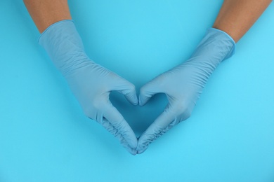 Photo of Person in medical gloves making heart with hands on light blue background, top view