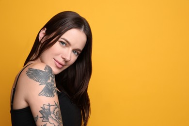 Beautiful woman with tattoos on arm against yellow background. Space for text