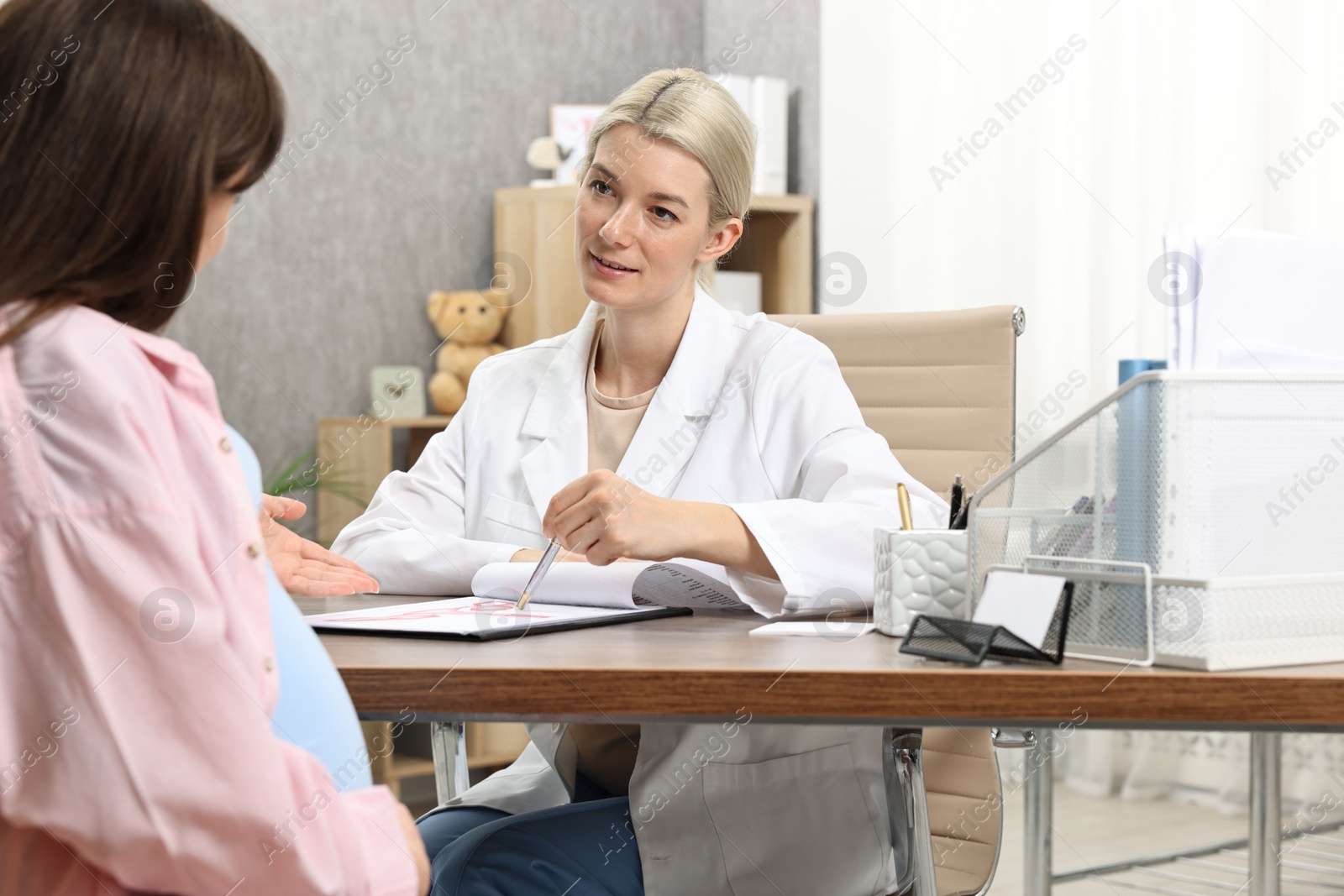 Photo of Doctor consulting pregnant patient at table in clinic