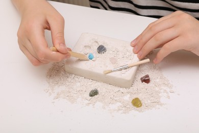 Photo of Child playing with Excavation kit at white table, closeup. Educational toy for motor skills