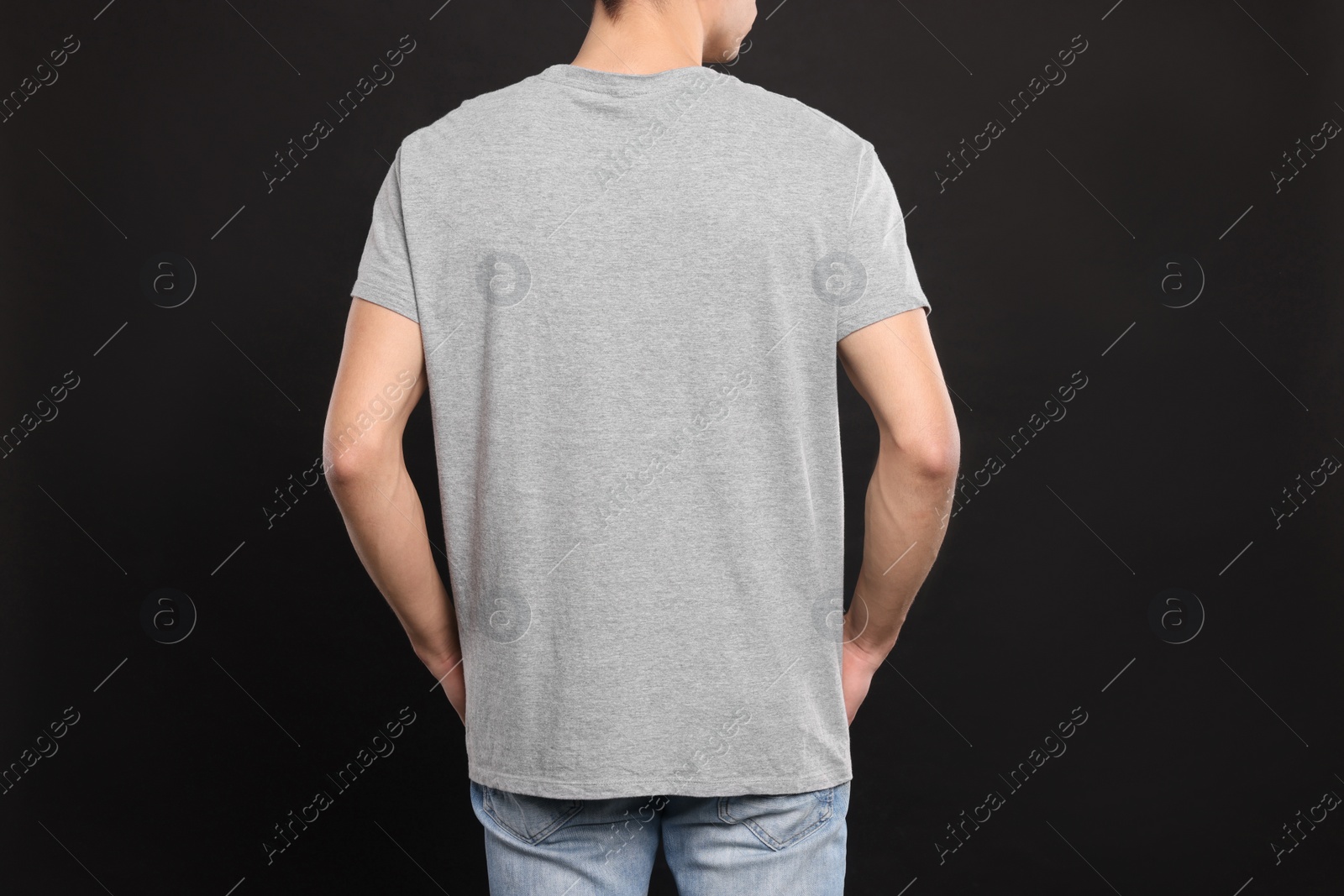 Photo of Man wearing light gray t-shirt on black background, back view. Mockup for design