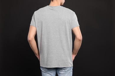 Man wearing light gray t-shirt on black background, back view. Mockup for design