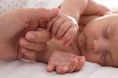 Photo of Mother with her cute sleeping baby on bed, closeup of hands