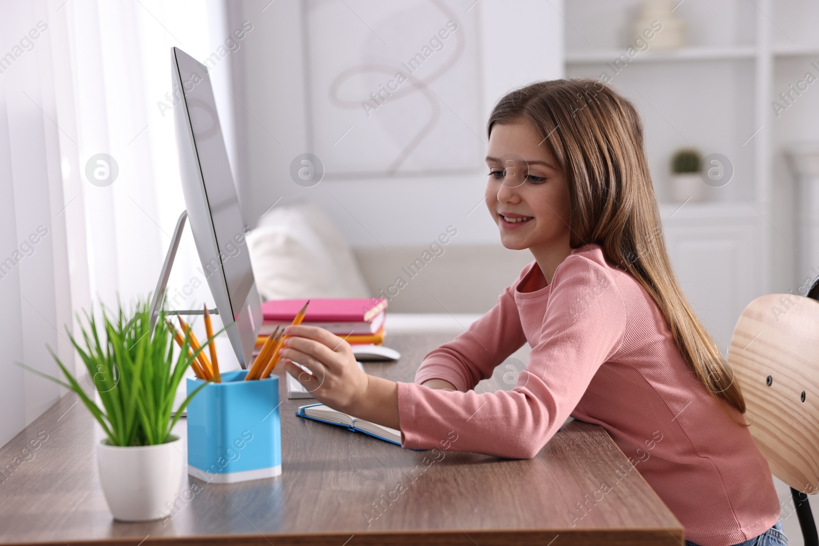 Photo of E-learning. Cute girl using computer during online lesson at table indoors