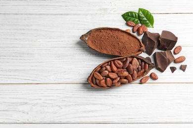 Flat lay composition with cocoa pods and chocolate on white wooden table. Space for text