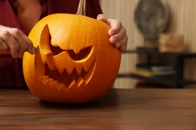 Photo of Woman carving pumpkin for Halloween at wooden table indoors, closeup
