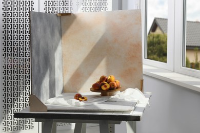 Photo of Stand with juicy peaches and double-sided backdrops on table in photo studio