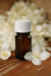Photo of Bottle of jasmine essential oil and white flowers on wooden table, closeup