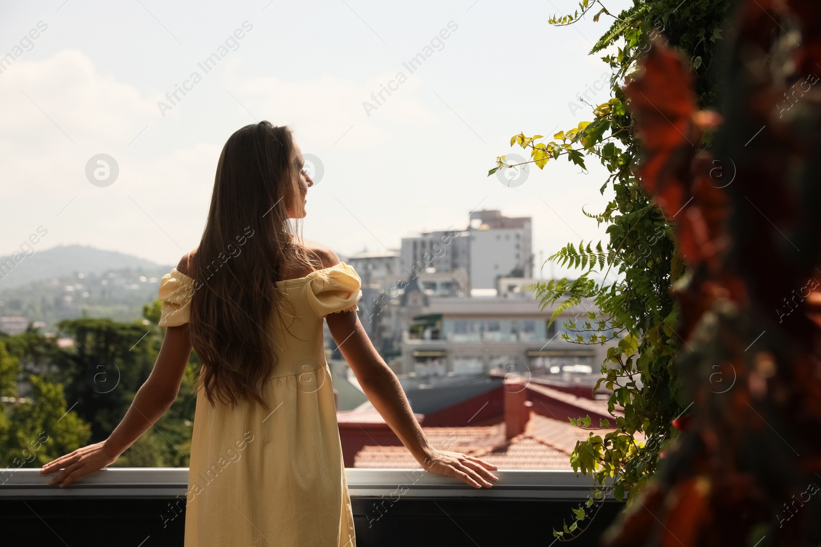 Photo of Young woman standing on balcony, back view. Space for text