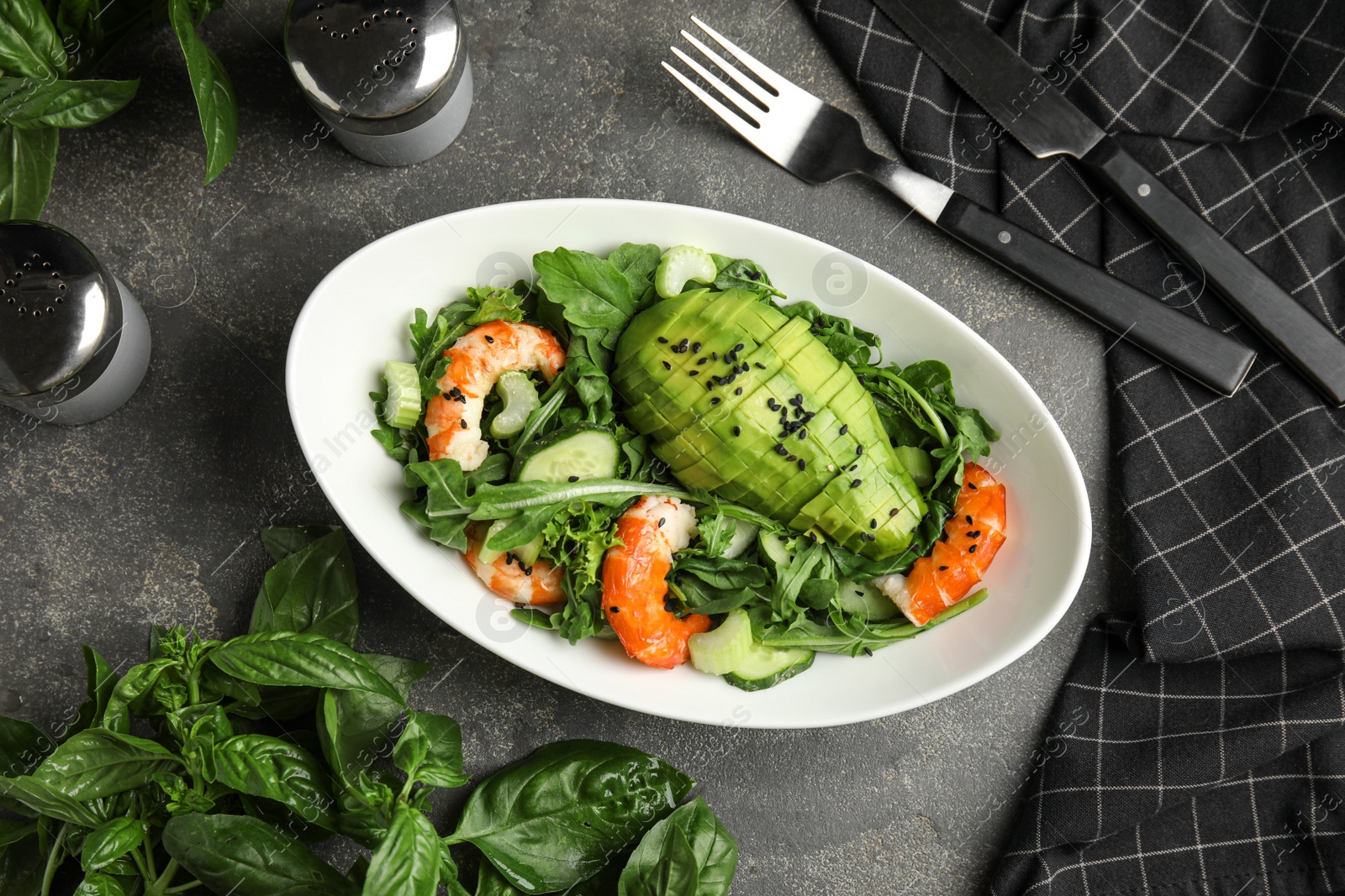 Photo of Delicious avocado salad with shrimps in bowl on grey table, flat lay