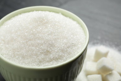Photo of Granulated sugar in bowl on dark grey table, closeup