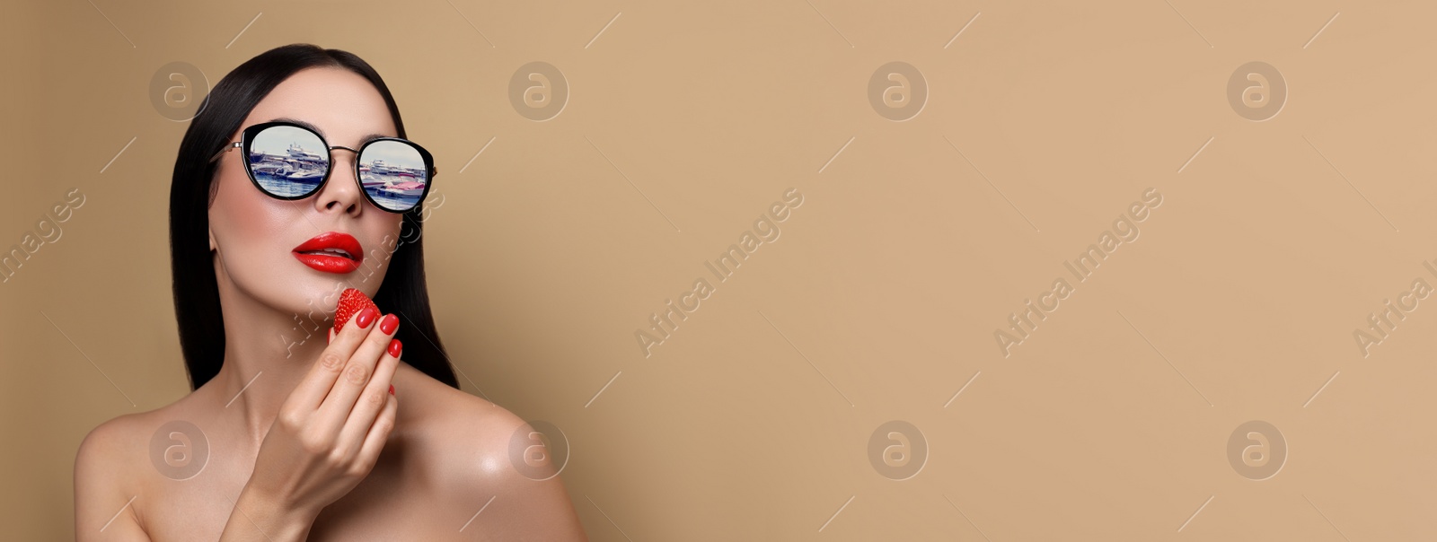 Image of Attractive woman in stylish sunglasses holding strawberry on dark beige background, space for text. Yachts reflecting in lenses. Banner design