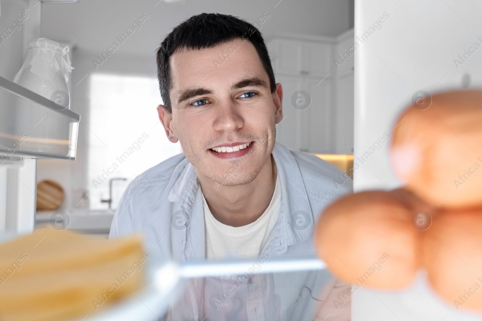 Photo of Happy man near refrigerator in kitchen, view from inside