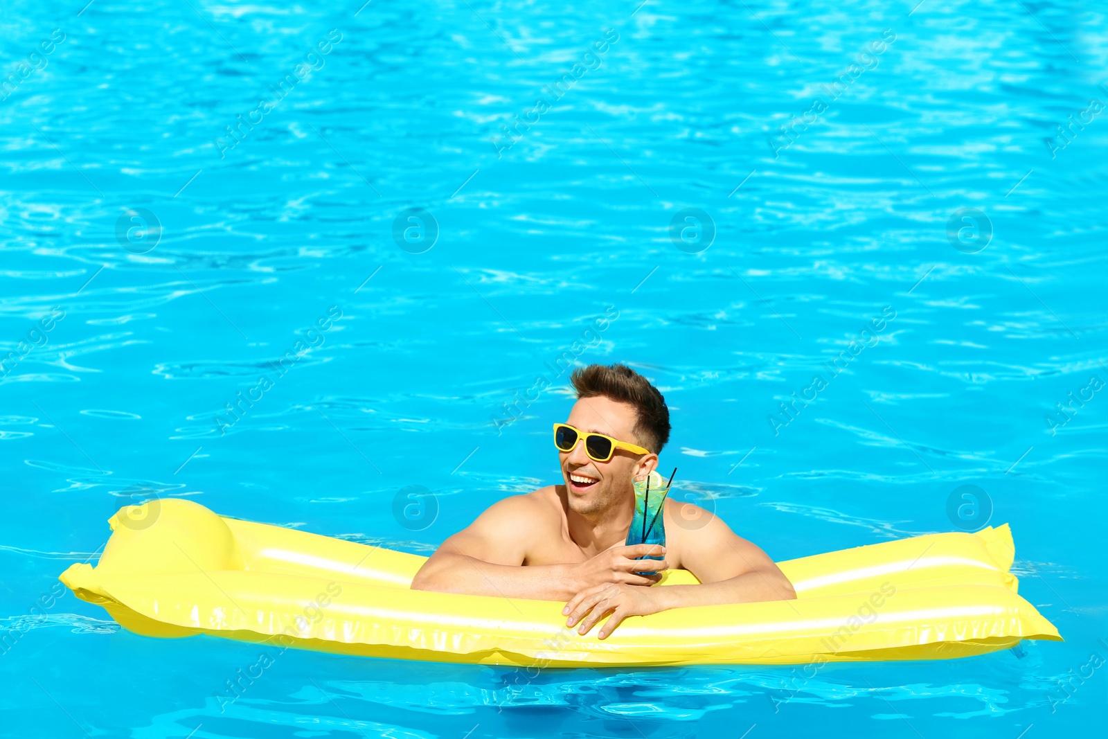Photo of Happy young man with cocktail and inflatable mattress in swimming pool