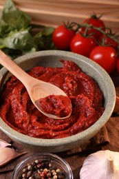 Bowl of tasty tomato paste with spoon and ingredients on table