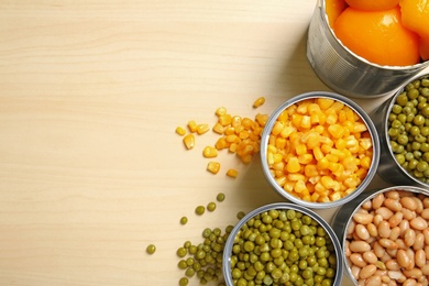 Open tin cans of conserved vegetables on wooden background, flat lay with space for text