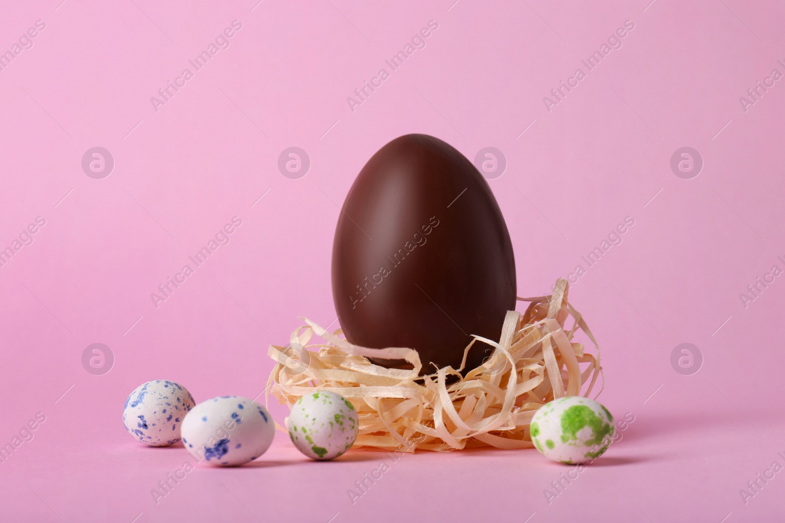 Photo of Decorative nest with tasty chocolate egg and candies on pink background