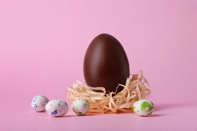 Photo of Decorative nest with tasty chocolate egg and candies on pink background