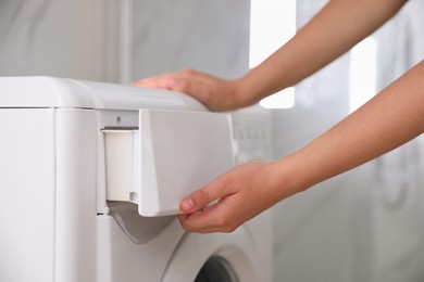 Photo of Woman opening detergent drawer of modern washing machine in bathroom, closeup