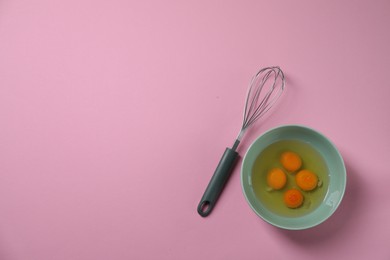 Photo of Metal whisk and raw eggs in bowl on pink background, flat lay. Space for text