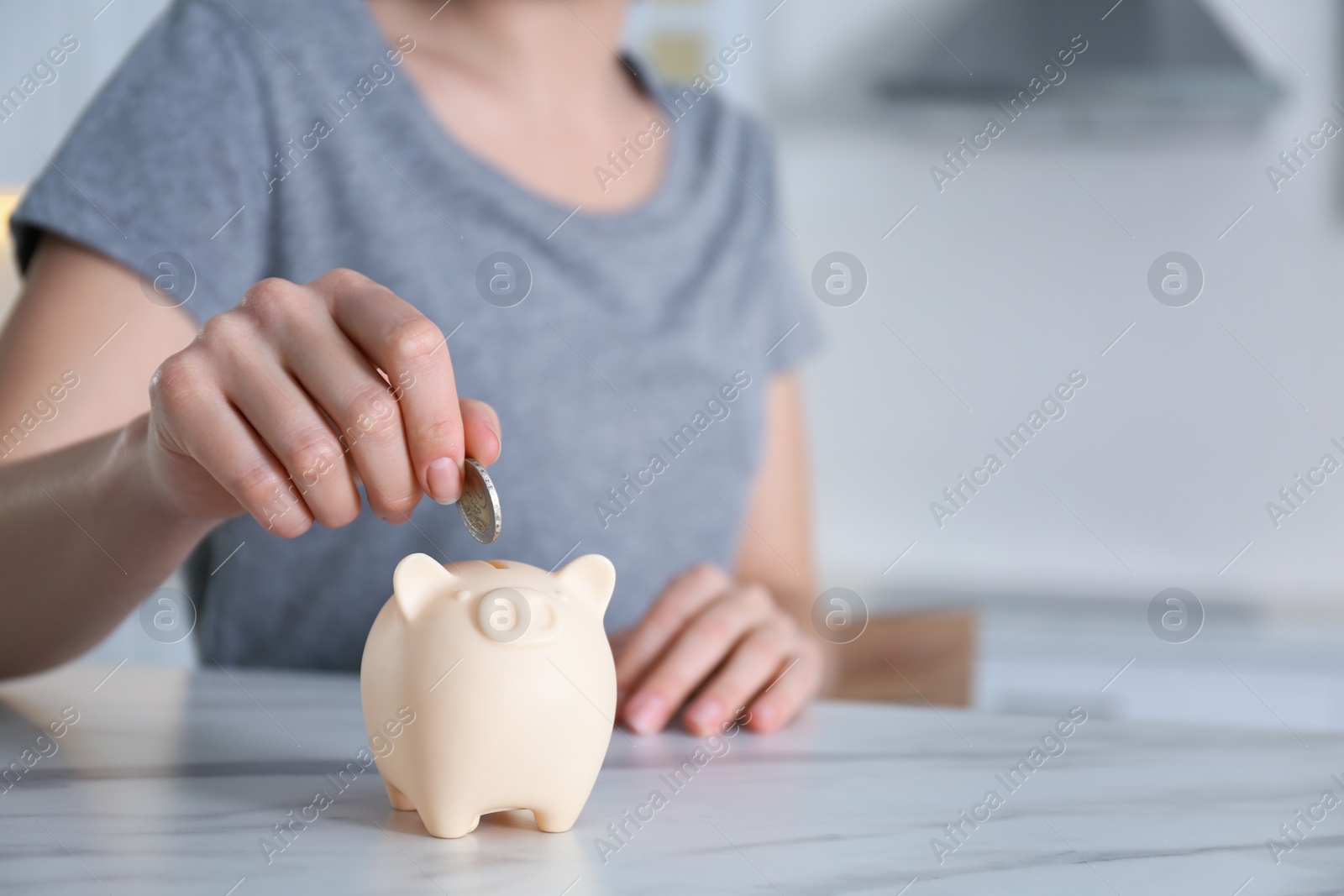 Photo of Woman putting money into piggy bank at marble table indoors, closeup